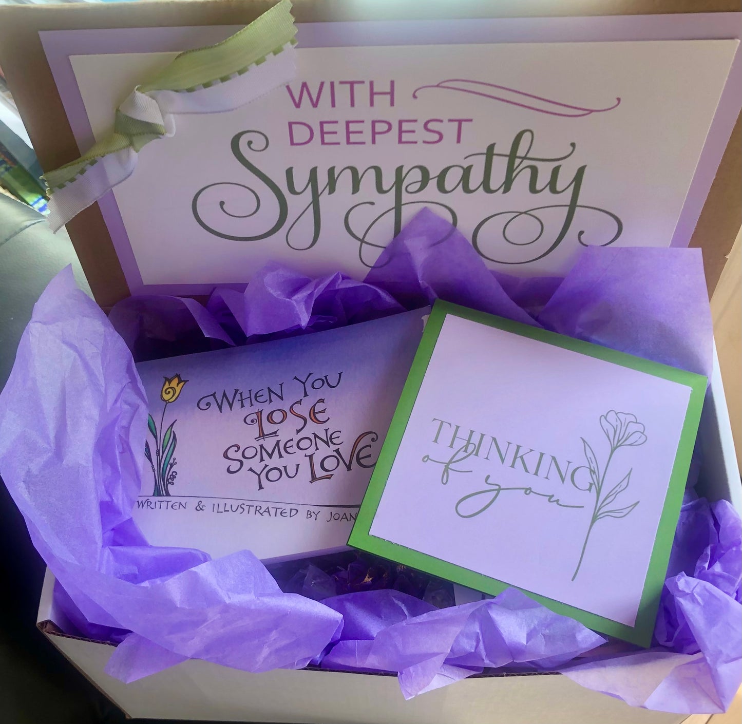 A sympathy package gift box with a card, purple tissue paper, and a decorative ribbon, featuring Sympathy messages.