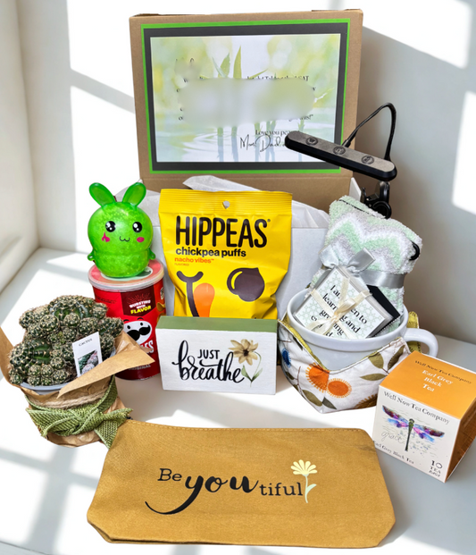 Gift basket with various items including a plant, snacks, and a motivational card on a white surface.