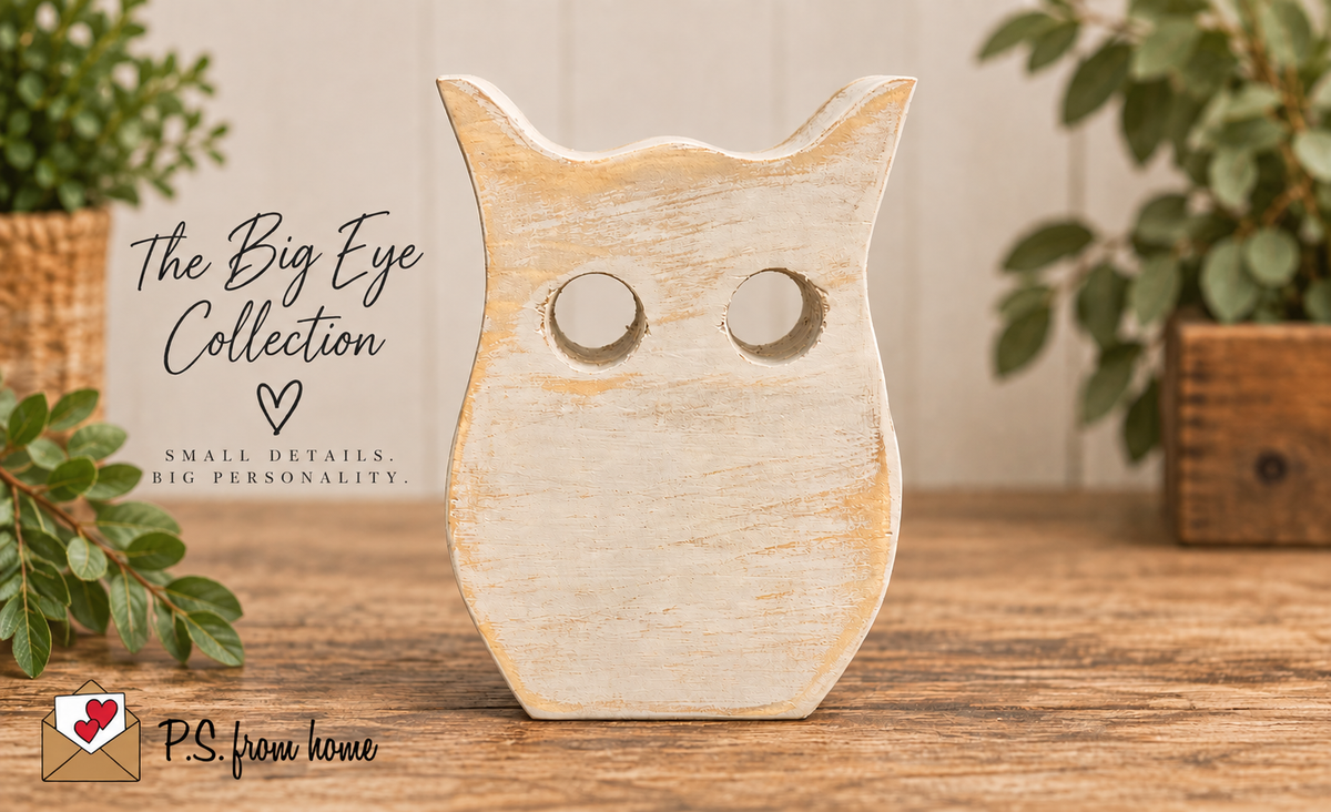 A rustic wooden owl figurine with distressed beige and light brown tones, featuring large circular eye cutouts, displayed on a wooden surface with decorative plants in the background. Text overlays on the left read 'The Big Eye Collection' and 'P.