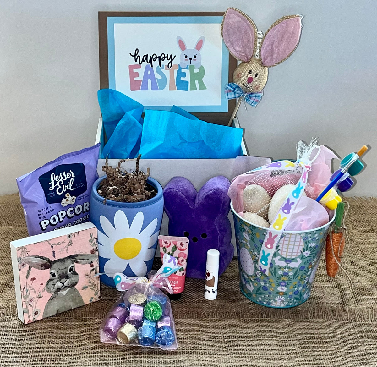 A collection of Easter-themed items including a bunny-themed popcorn bucket, chocolate eggs, a framed 'Happy Easter' sign, and other assorted Easter treats.
