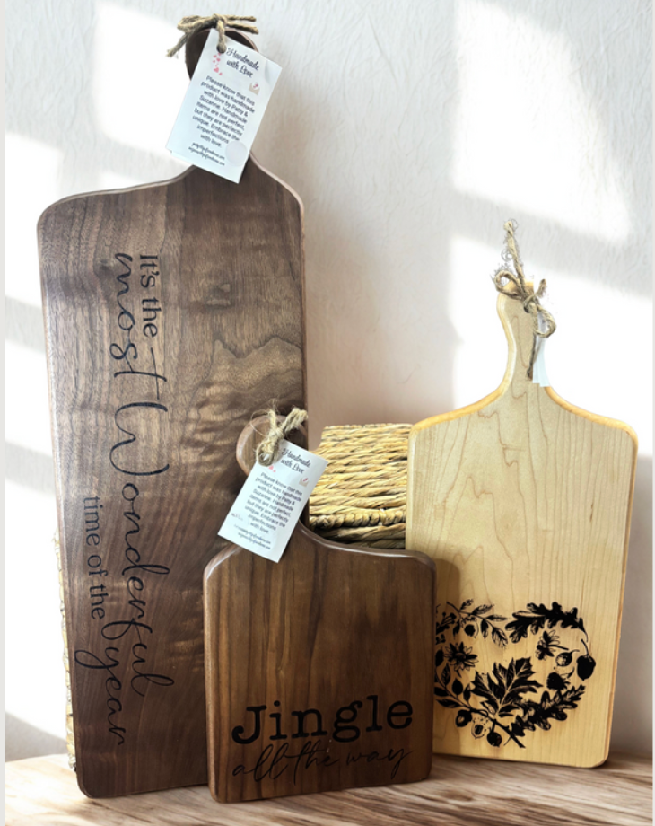 Three wooden cutting boards with engraved text and designs on a neutral background