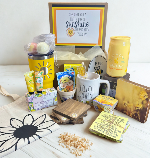 Gift box with 'Sending you a little box of sunshine' card, mug, and various items on a white surface.
